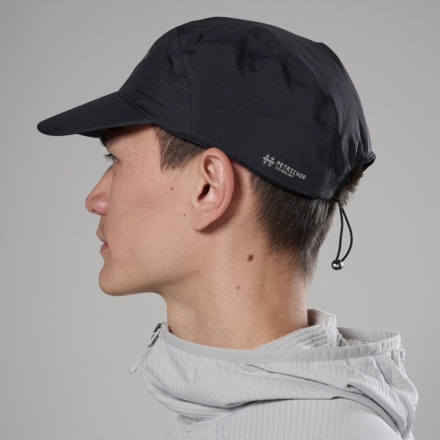 Person wearing a black cap with a brand logo on a gray background