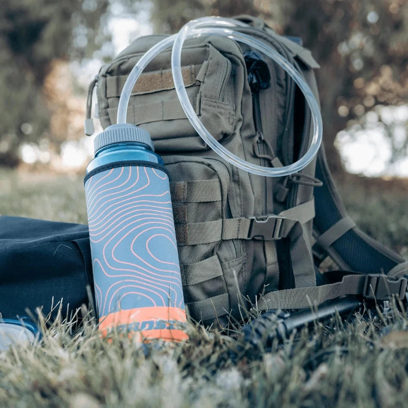  Water bottle with blue and orange sleeve, a gray cap and white straw on a green backpack in a natural setting.
