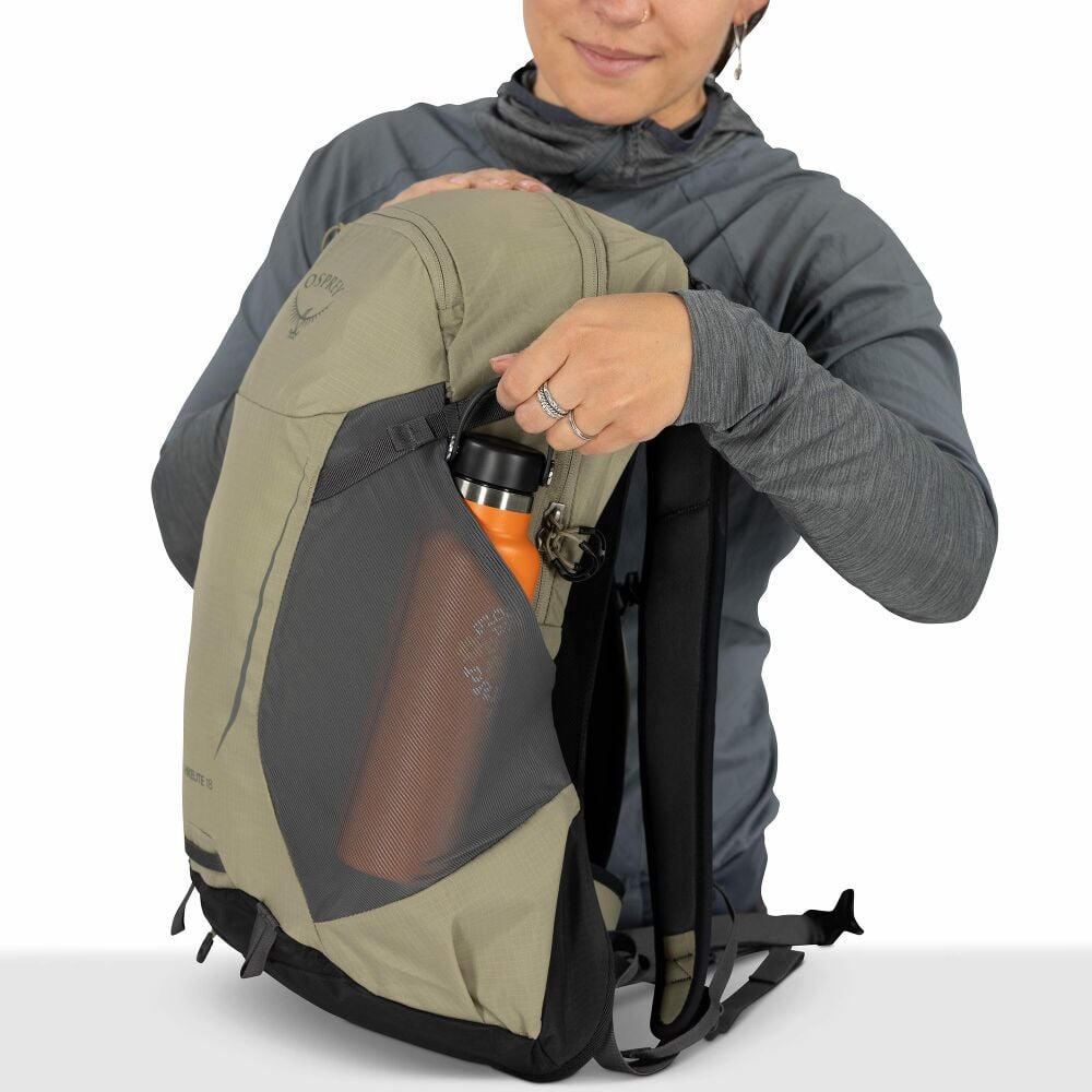 Person holding a beige backpack with a water bottle in the side pocket 