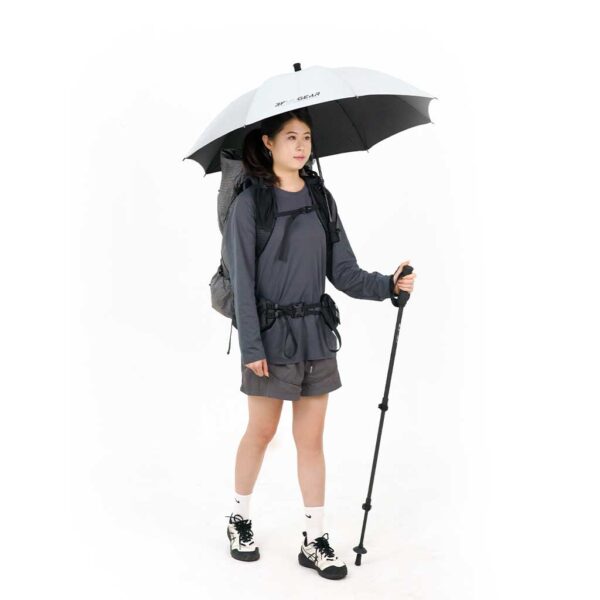 Woman in hiking gear holding an umbrella and walking stick on a white background