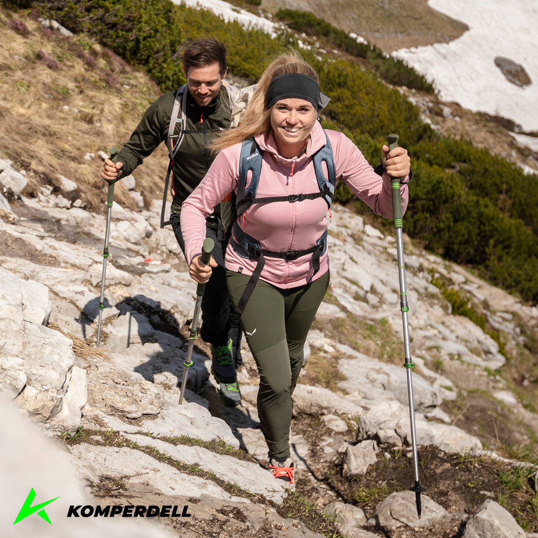 Two hikers on a rocky hill side with green and silver trekking poles, Komperdell logo in corner