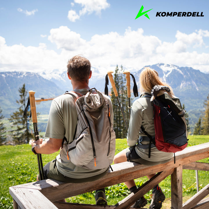 Two hikers sitting on a porch railing holding trekking poles and looking at mountains