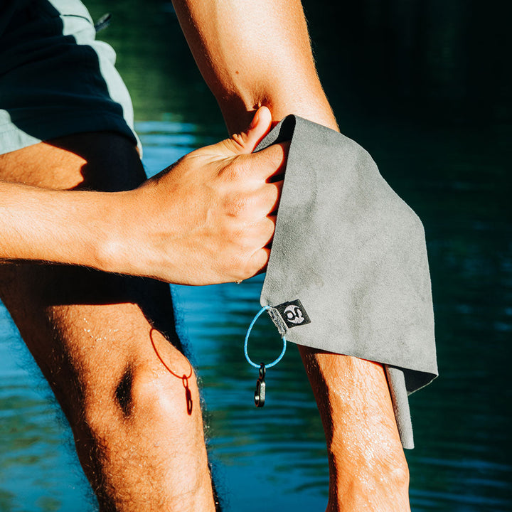 Person using a small grey towel by a body of water