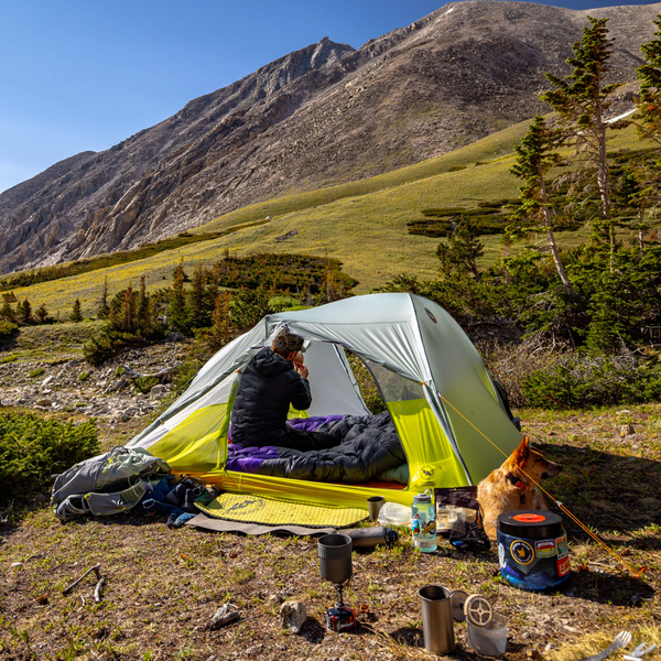 Person camping in a mountainous area with a tent and cooking equipment.