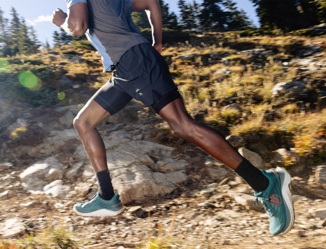 Person running on a rocky trail with trees in the background wearing teal running shoes