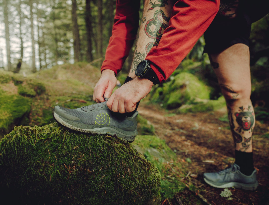 Person tying a grey running shoe in a forest setting