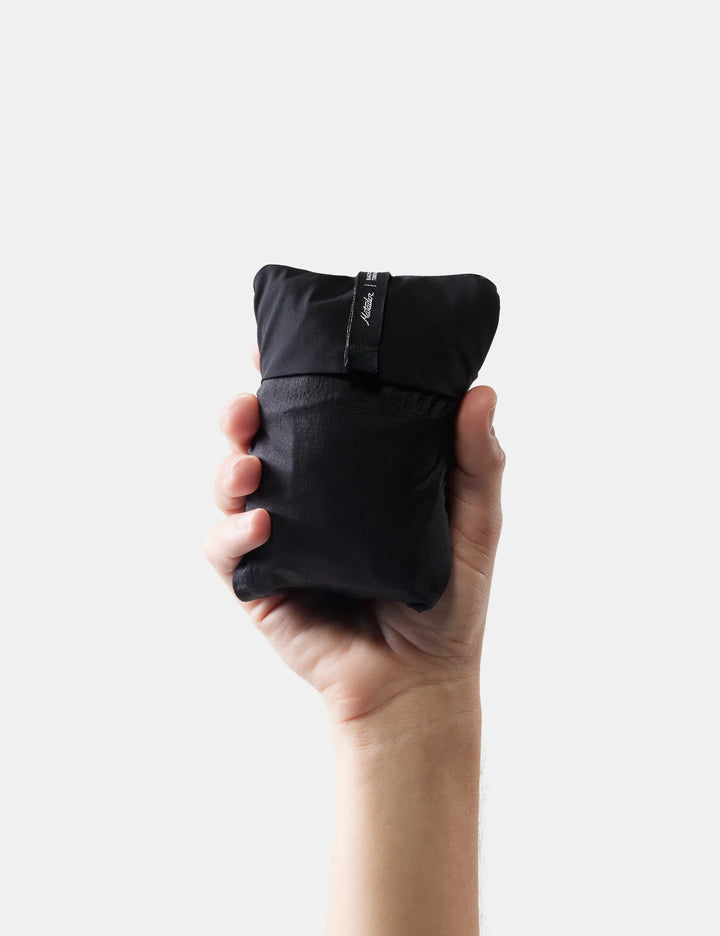 Hand holding a black travel pillow that is packed up into small pouch against a white background