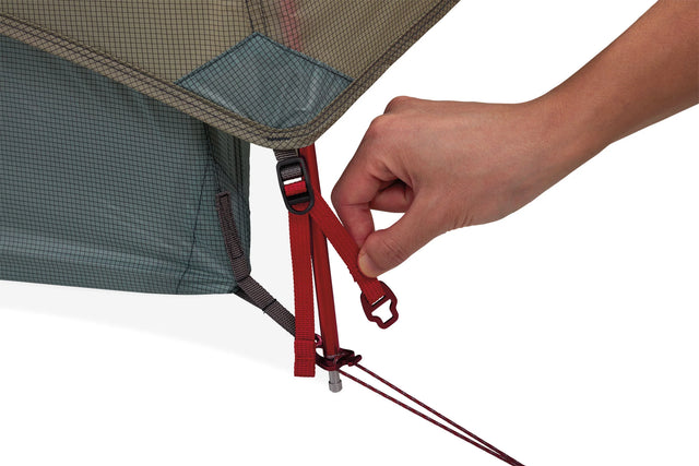 Hand adjusting a red strap on a grey and tan tent