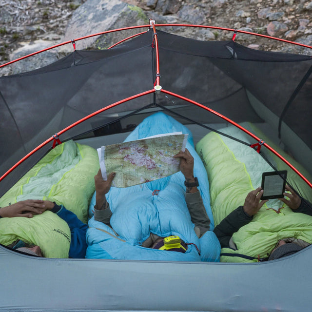People inside a tent using maps and digital devices, surrounded by nature.