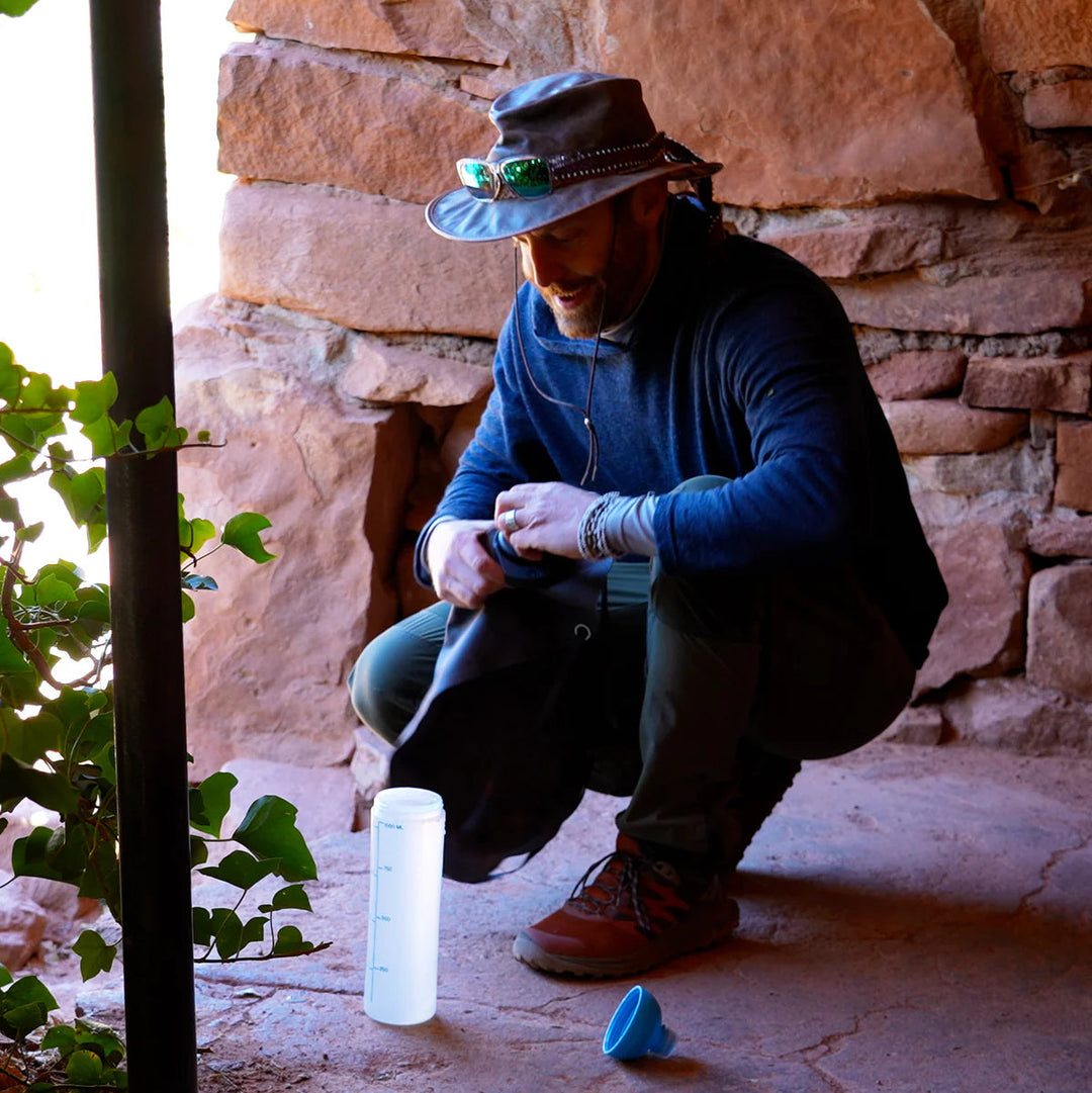 Man crouching in a shady urban environment, filling a water bottle 