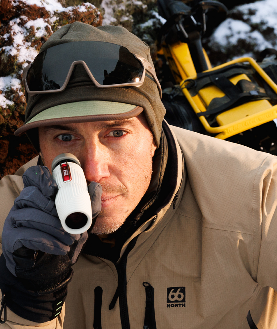 Man in winter clothing looking through a monocular on a snowy background