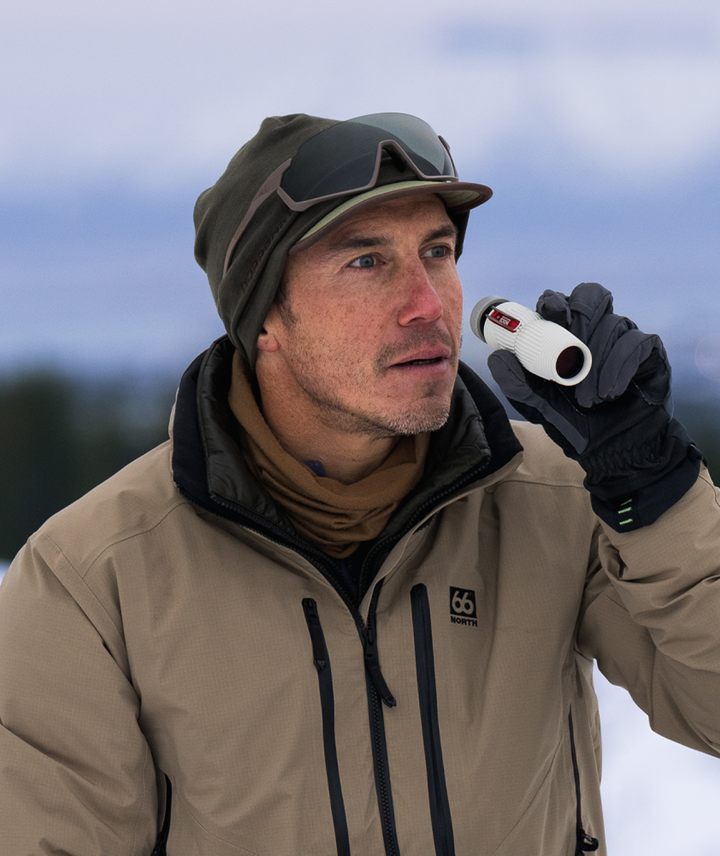 Man in winter clothing holding a monocular against a snowy background