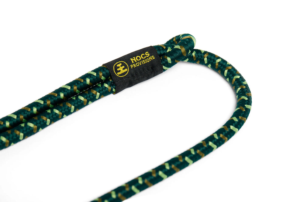 A close-up of a dark green and light green braided rope with a black woven label that reads 'NOCS PROVISIONS' in yellow, set against a solid white background.
