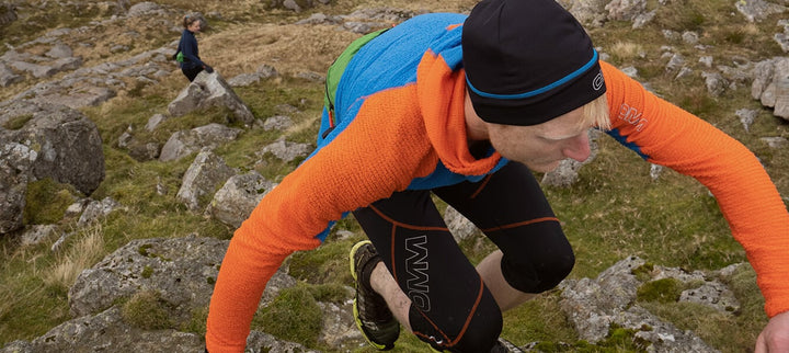 Person in blue and orange hoodie runs up hill on a steep rocky slope