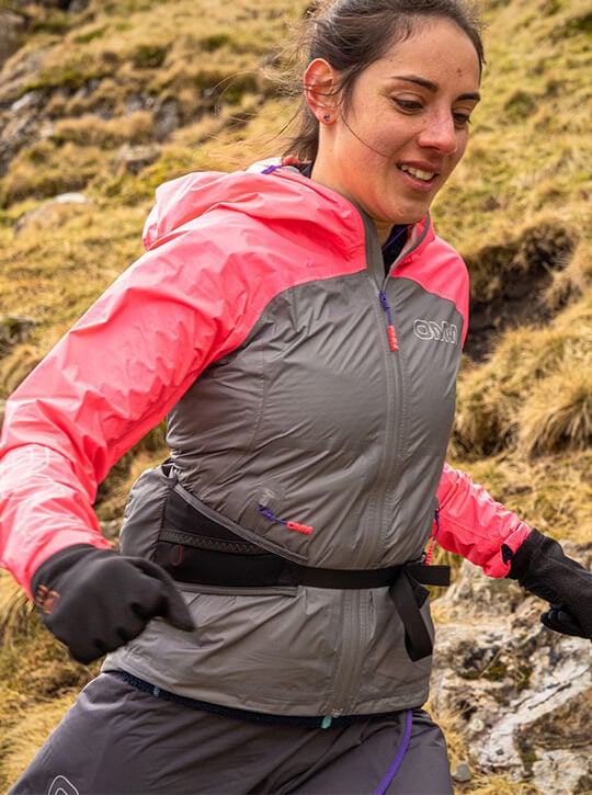 Woman wearing a pink and grey waterproof jacket running on a rocky terrain