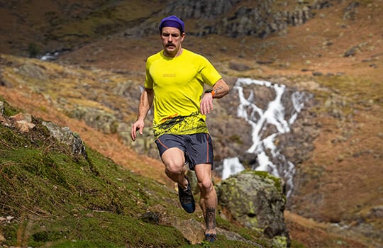 Man wearing shorts running on a mountain trail with a scenic background