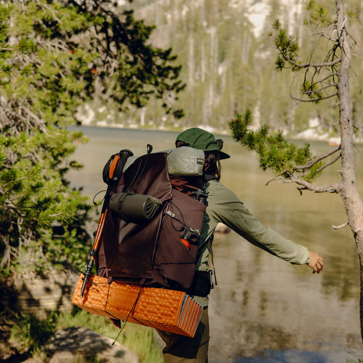 Person with a large backpack standing by a lake with trees in the background