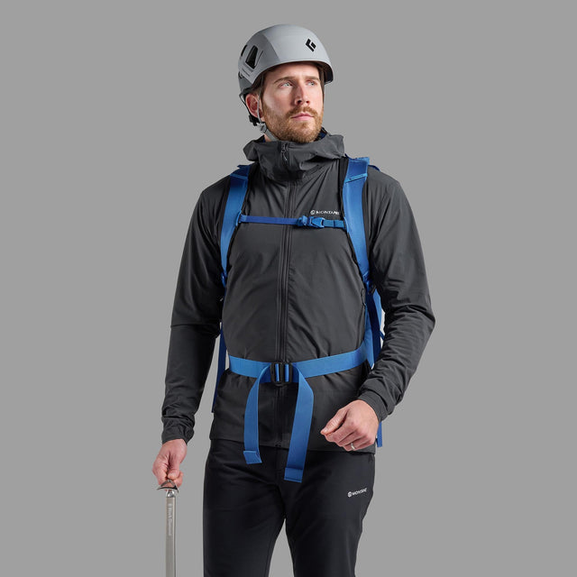 Man wearing a black jacket and helmet with a blue backpack on a gray background
