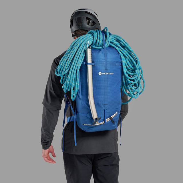 Person wearing a blue Montane backpack with climbing gear on a gray background