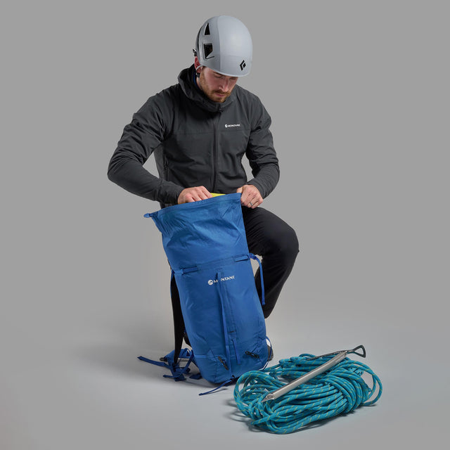 Person unpacking a blue backpack with climbing gear on a gray background