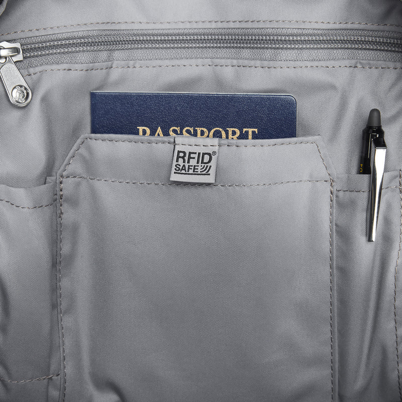 Close-up of a light gray backpack pocket with a blue passport inserted and a black pen in the side pocket. A fabric label on the pocket reads &