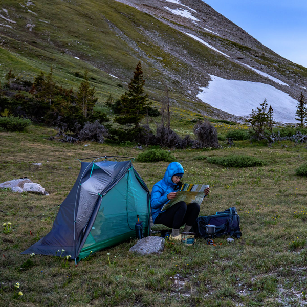 Person camping in a mountainous area, sitting by a tent and reading a map.