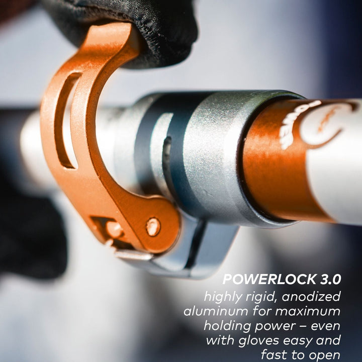 Close-up of a POWERLOCK 3.0 anodized aluminum locking tool on a metal handlebar, with a gloved hand holding the orange anodized clamp and white text overlay describing its features.