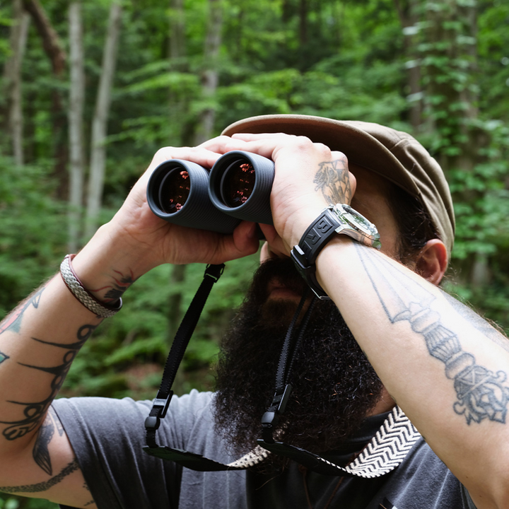 Person with tattoos using binoculars in a forest setting