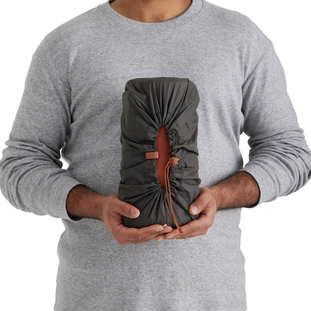 Person holding a grey stuff sack containing an orange sleeping mat