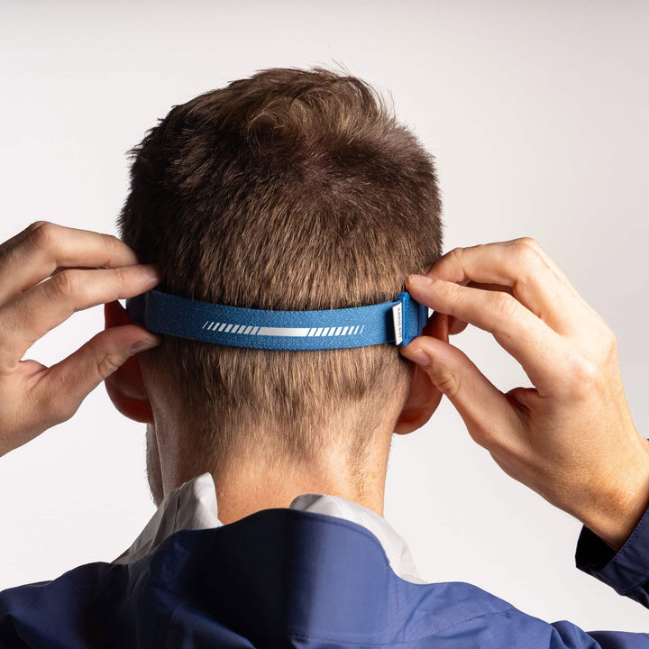 Person wearing a blue headlamp on a plain background