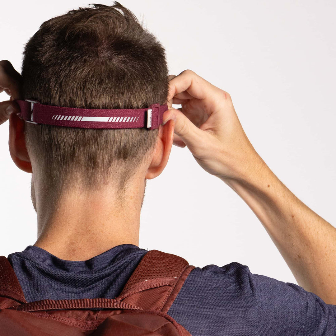 Person adjusting a maroon headlamp on a plain background