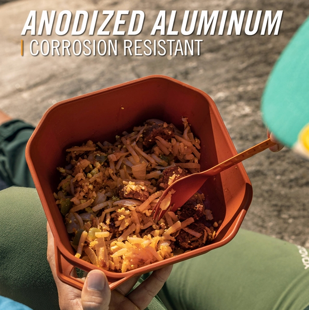 A person holds an anodized aluminum hexagonal food container filled with rice and meat, with a matching spoon resting inside. The image includes text overlay reading &