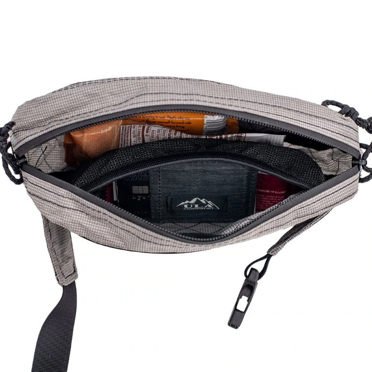 An open gray and black checkered crossbody bag showing its interior storage compartments, zipper, and a black zippered pouch with a visible logo.