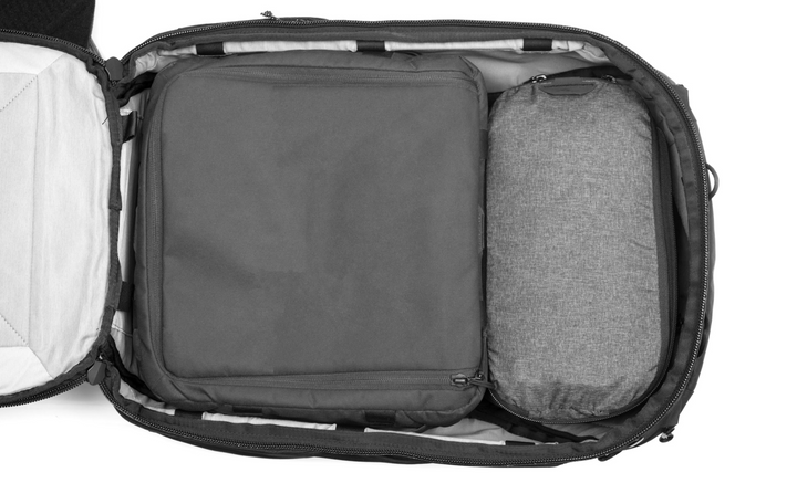 An open backpack shown from above, revealing a dark gray padded compartment and a gray zippered pouch inside, on a white background.