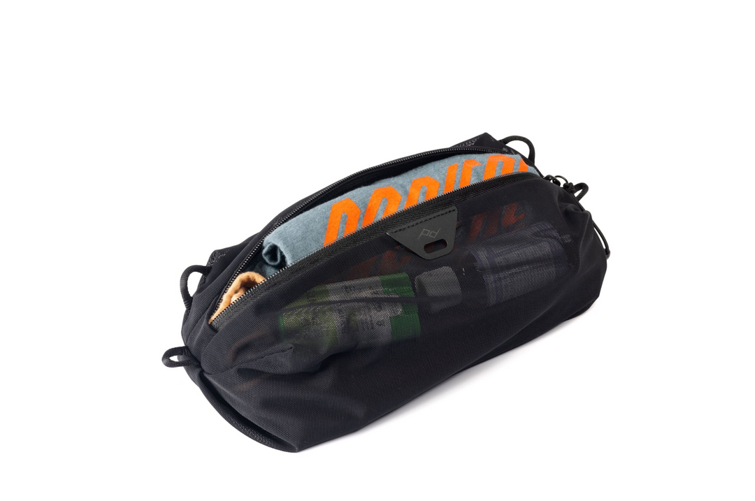 A black zippered utility pouch shown open on a plain white background, with a blue and orange garment and other items partially visible inside.