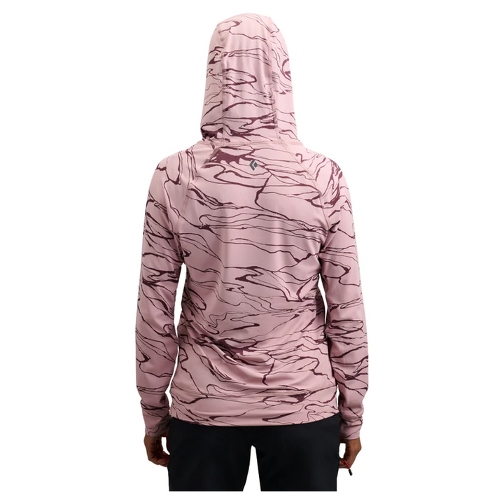A woman viewed from the back wearing a hooded long-sleeve athletic top with a pink and mauve abstract marbled pattern, paired with black bottoms, on a plain white background.