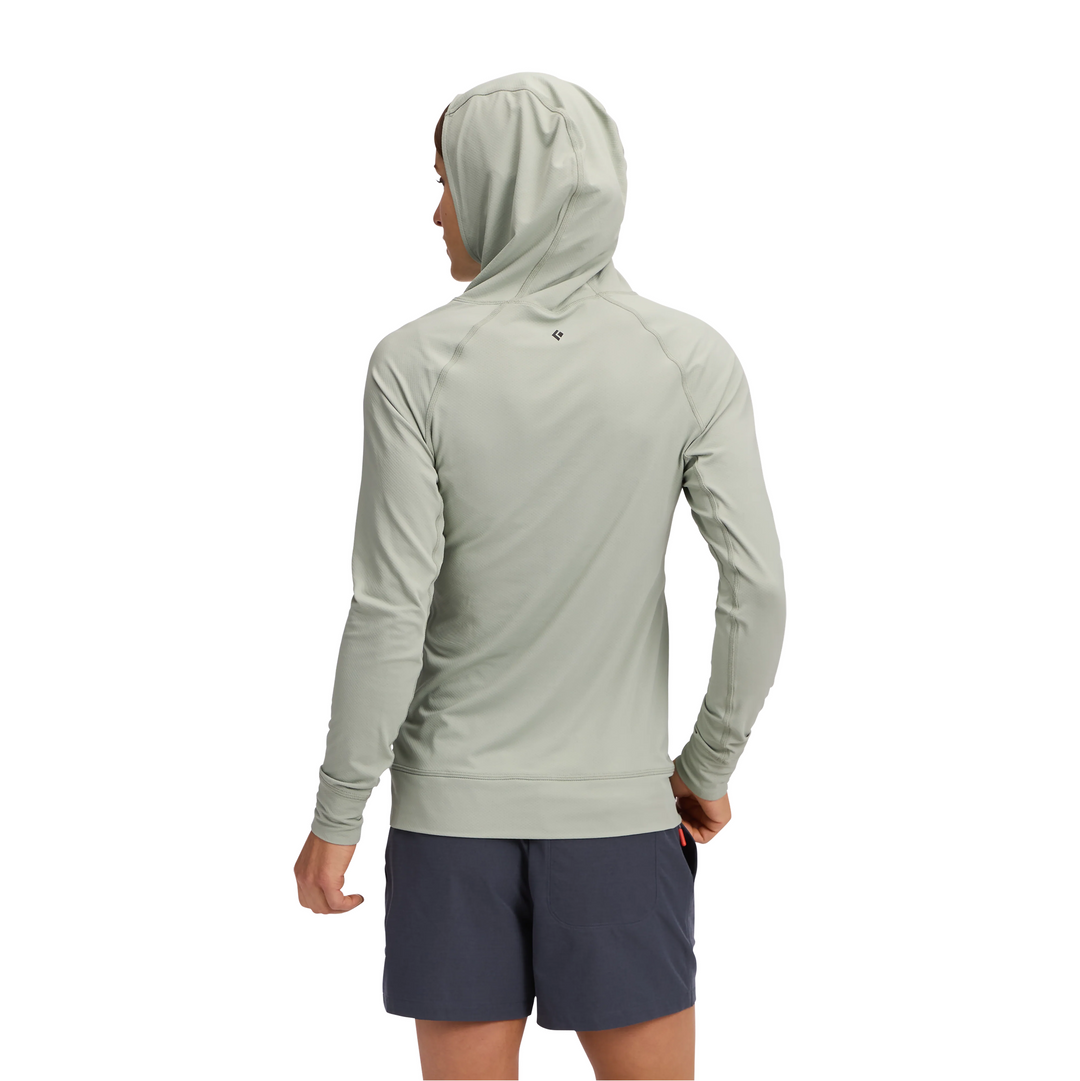 A man wearing a light sage green hooded long-sleeve athletic shirt and navy blue shorts, shown from the back against a plain white background.
