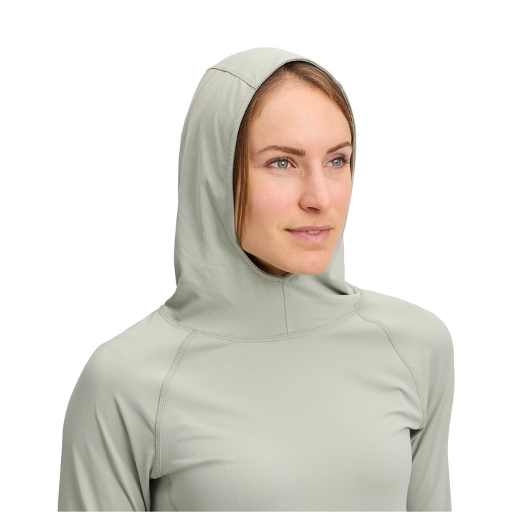 A woman wearing a light sage green hooded long-sleeve athletic top, shown from the chest up against a plain white background.