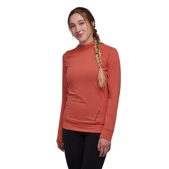 A woman with blonde hair in a braid wearing a long-sleeve, mock-neck athletic top in a muted terracotta orange color, paired with black leggings, against a plain white background.