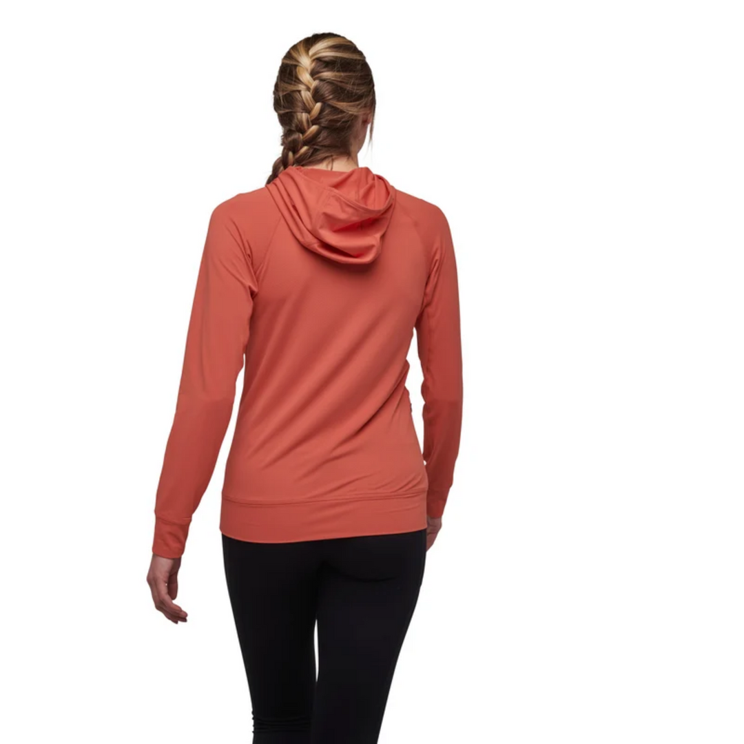 A woman viewed from behind wearing a long-sleeve hooded athletic top in a muted terracotta or burnt orange color, paired with black leggings, against a plain white background.