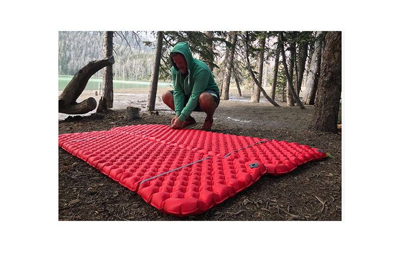 Person securing two red hiking matresses together with elastic loops in the forest