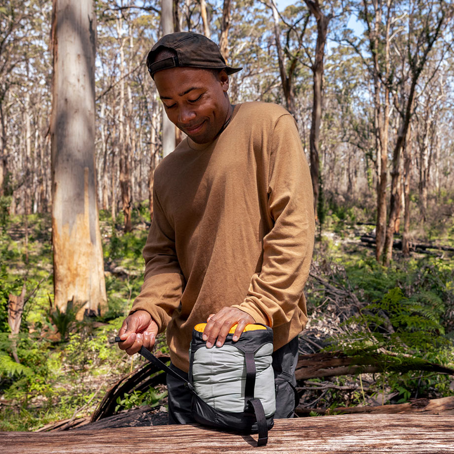 Person in a forest setting tightening the straps on a compression sack