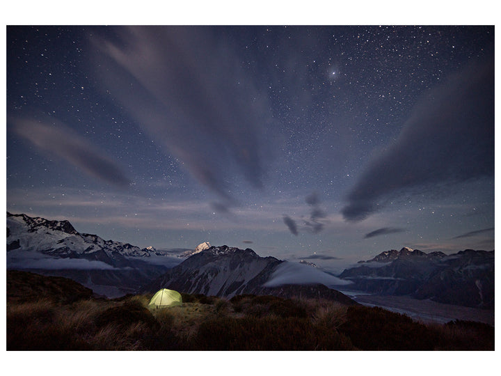 Green hiking tent glowing from within with mountains and a starry sky
