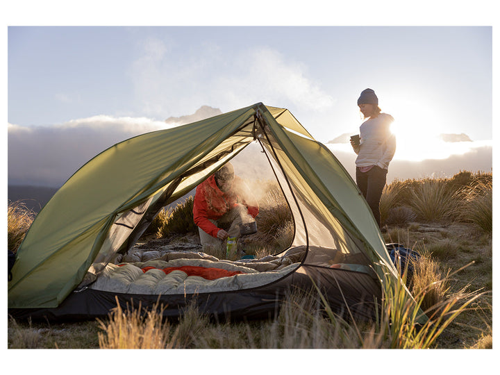 Two people with a tent among tussock with mountains in the background