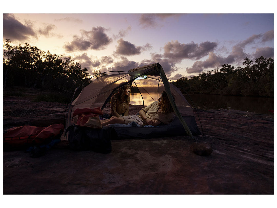 Two people in a hiking tent with fly rolled back at dusk on a beach