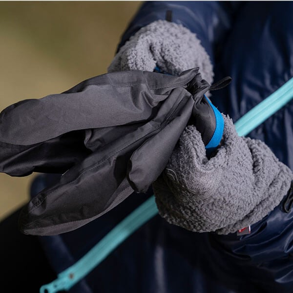 Close up of a person hands wearing textured grey mittens, about to put on waterproof shell mittens