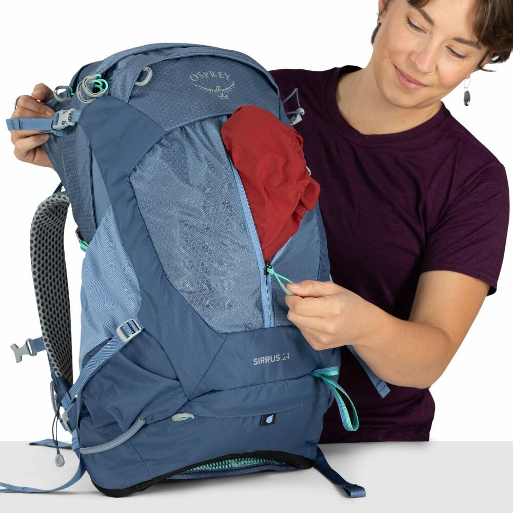 Person unzipping  the front zip on a blue Osprey Backpack