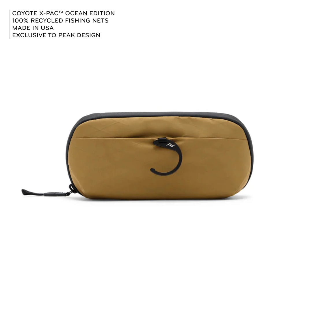Beige carrying case with black zipper on a white background, featuring text about recycled fishing nets and Peak Design.