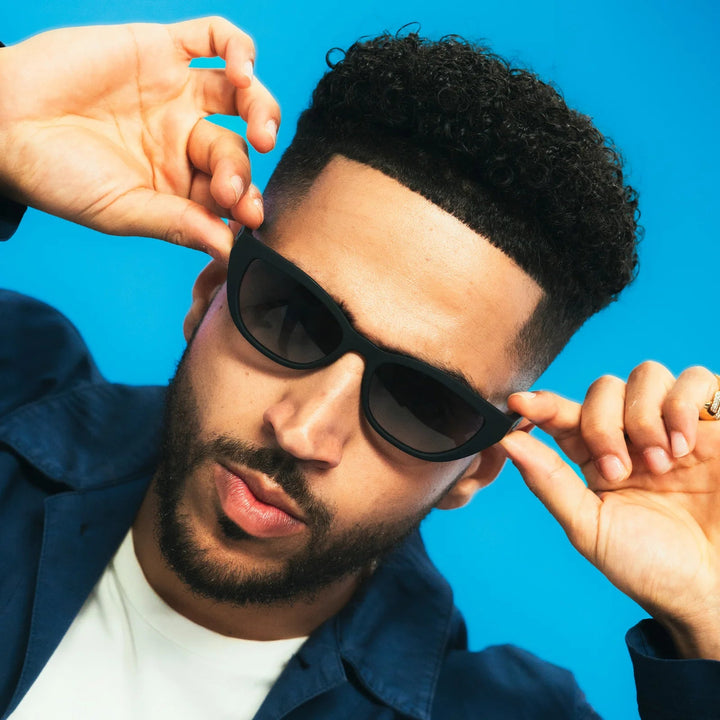 Man adjusting black sunglasses against a blue background