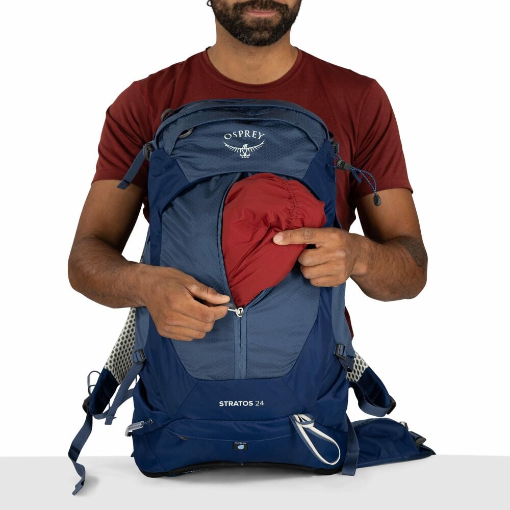 Person holding a blue Osprey backpack with a red item inside on a white background